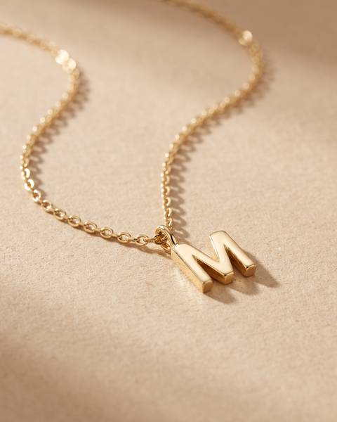 Collar Inicial con letra M en oro 18k sobre fondo arena
