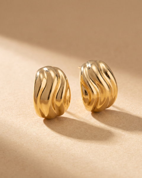 Pendientes Ola esculturales en oro 18k sobre fondo arena