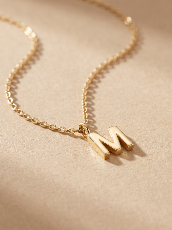 Collar Inicial con letra M en oro 18k sobre fondo arena