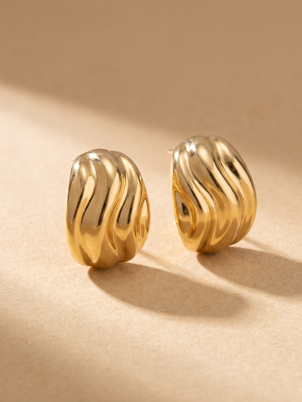 Pendientes Ola esculturales en oro 18k sobre fondo arena